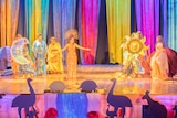 Women in colourful dresses on a stage with a brightly coloured, striped background