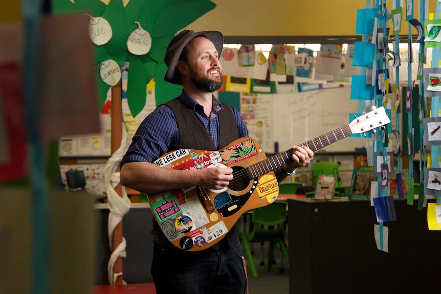 CJ Shaw holds a guitar in a classroom.