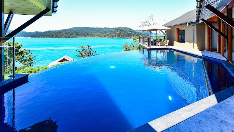 A spacious bedroom with glass walls overlooking crystal blue water.