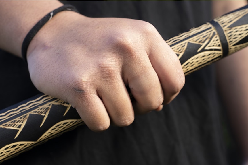 A hand is gripped around a beige wooden bar decorated in dark mountain shapes.