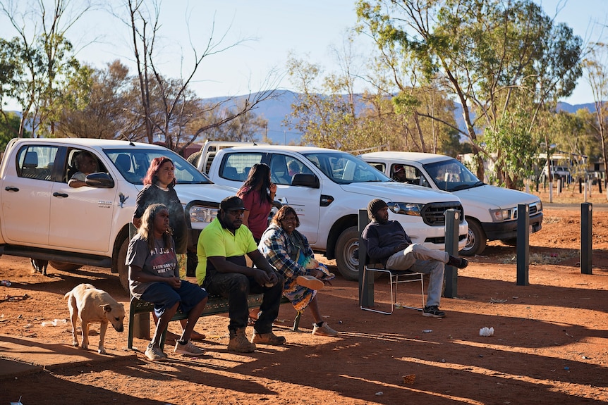 Haasts Bluff community members sit down in front of three white four-wheel-drives.