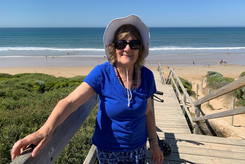 Sandra Bone wears a white hat, blue shirt and sunglasses on the steps to the beach at Ocean Grove.