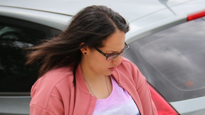 A woman in a pink jacket looks away from the camera as she walks down a suburban street.