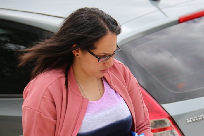 A woman in a pink jacket looks away from the camera as she walks down a suburban street.