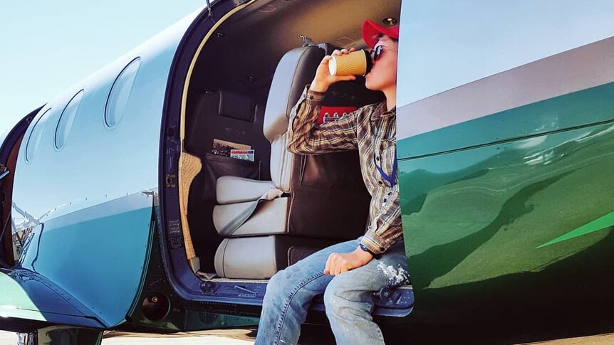 Woman sits in plane doorway having coffee
