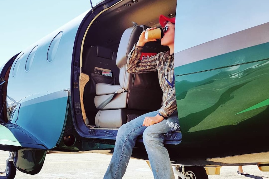 Woman sits in plane doorway having coffee