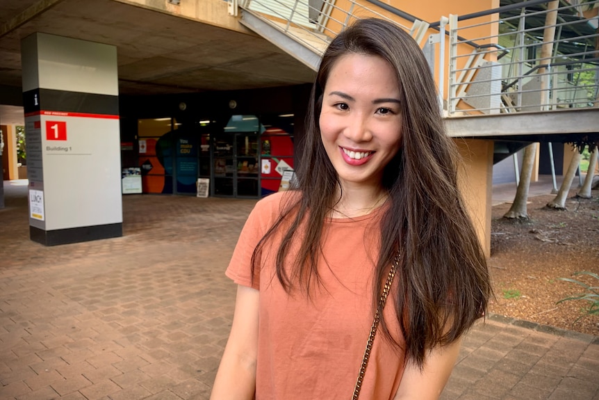 A woman on campus smiling to camera.