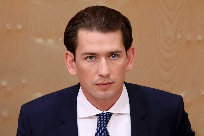 A close up of Sebastian Kurz wearing a dark blue suit and tie with brown hair and blue eyes.