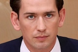 A close up of Sebastian Kurz wearing a dark blue suit and tie with brown hair and blue eyes.