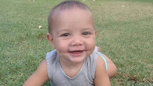 A photo of a happy smiling baby Charlie, lying on the grass and smiling at the camera.