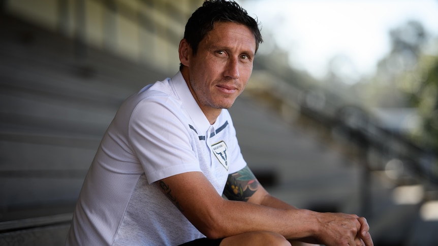 Mark Milligan sits in an empty grandstand and smiles for a profile photo