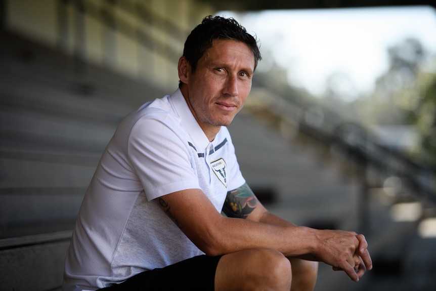 Mark Milligan sits in an empty grandstand and smiles for a profile photo