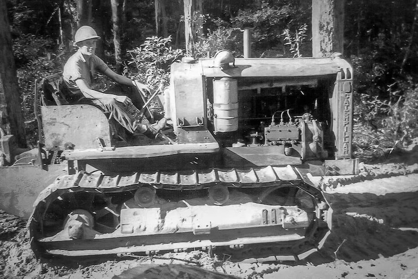 A black and white picture of a man sitting on a caterpillar machine