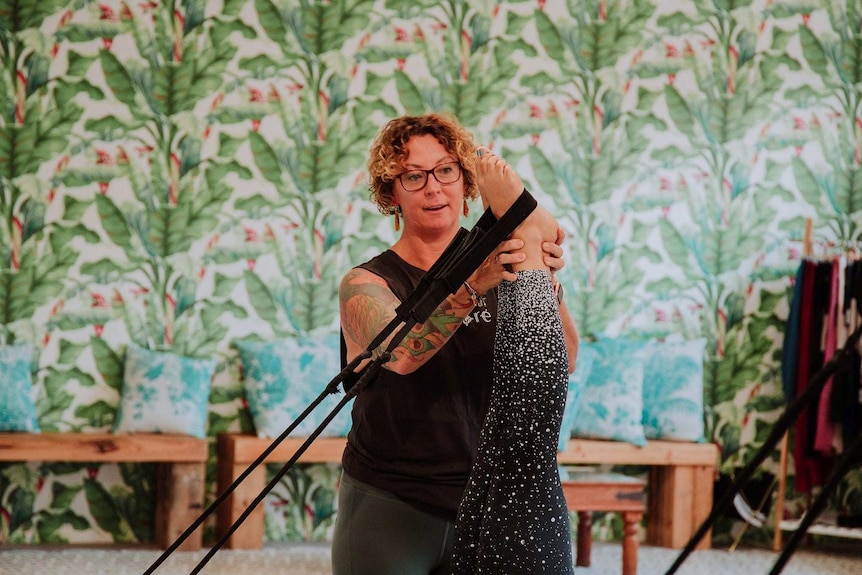 Woman with curly short hair and glasses corrects the technique of a another woman on a Pilates reformer bed.