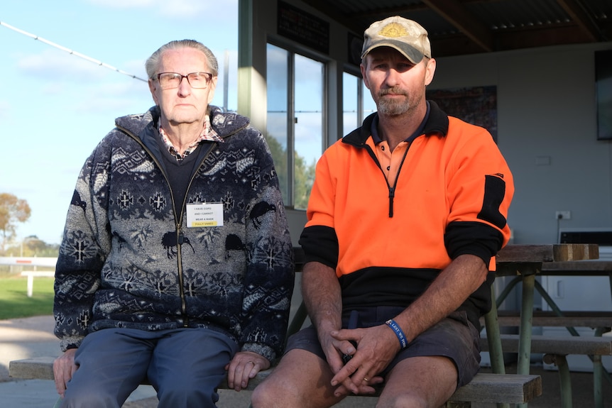 An elderly gentleman and his middle-aged son sit on a park bench at a caravan park. 