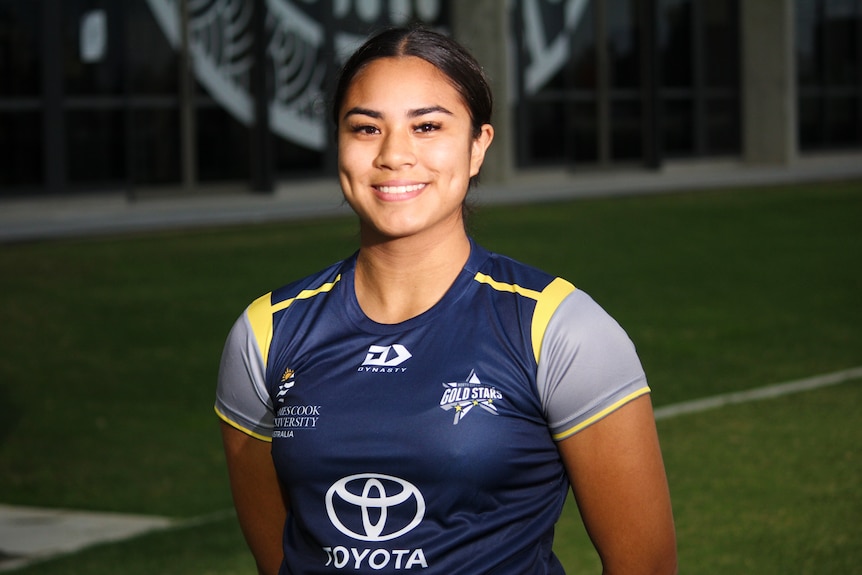 A woman wearing a jersey smiles on the edge of a football field