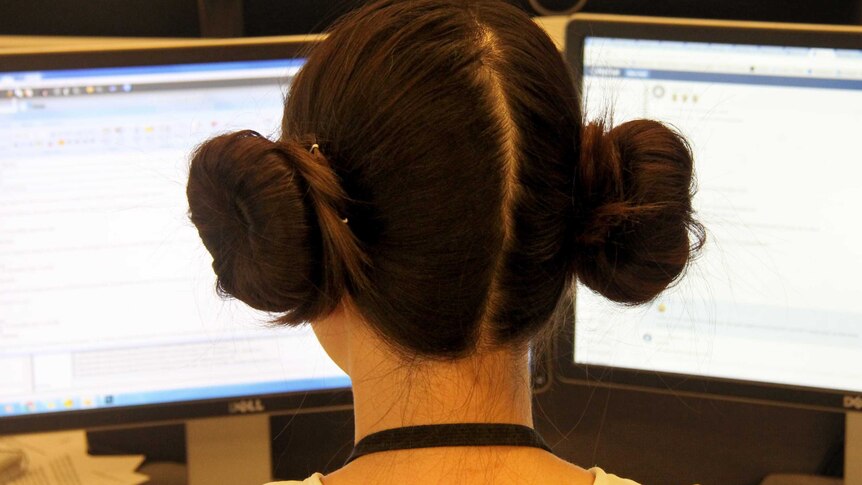Photo from behind of a woman with Princess Leia hair buns working at her computer.
