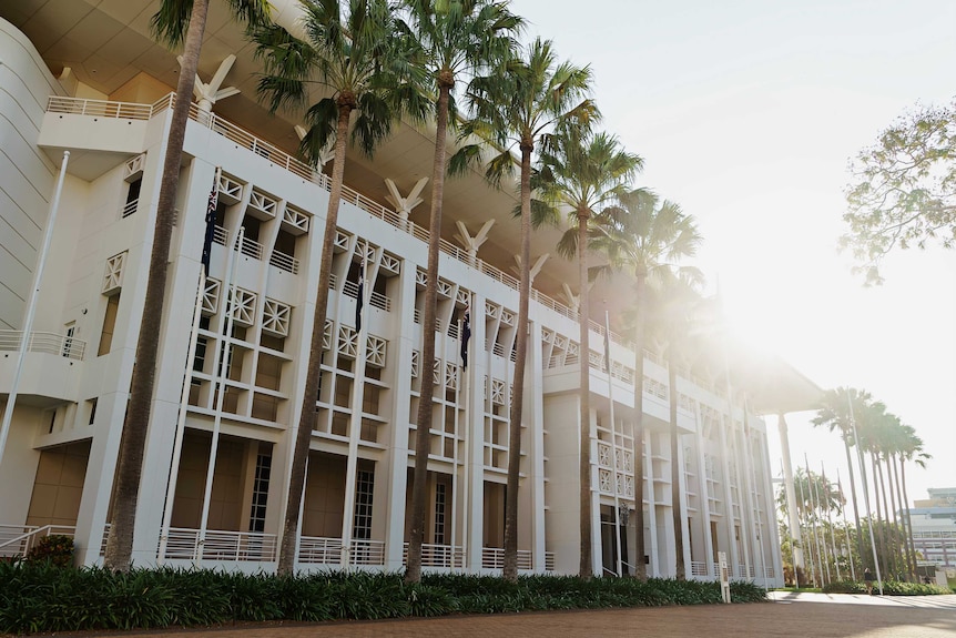 Une photo extérieure du Parlement à Darwin.  Il y a de grands palmiers à l'avant.