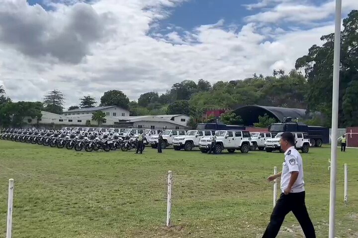 Dozens of motorcycles and SUVs parked on a sports field. 