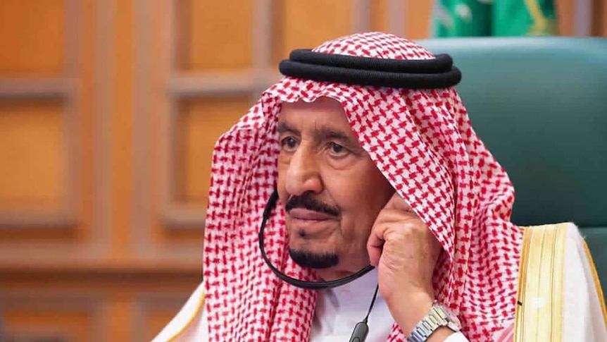 Saudi King Salman sits in a green chair wearing headphones.