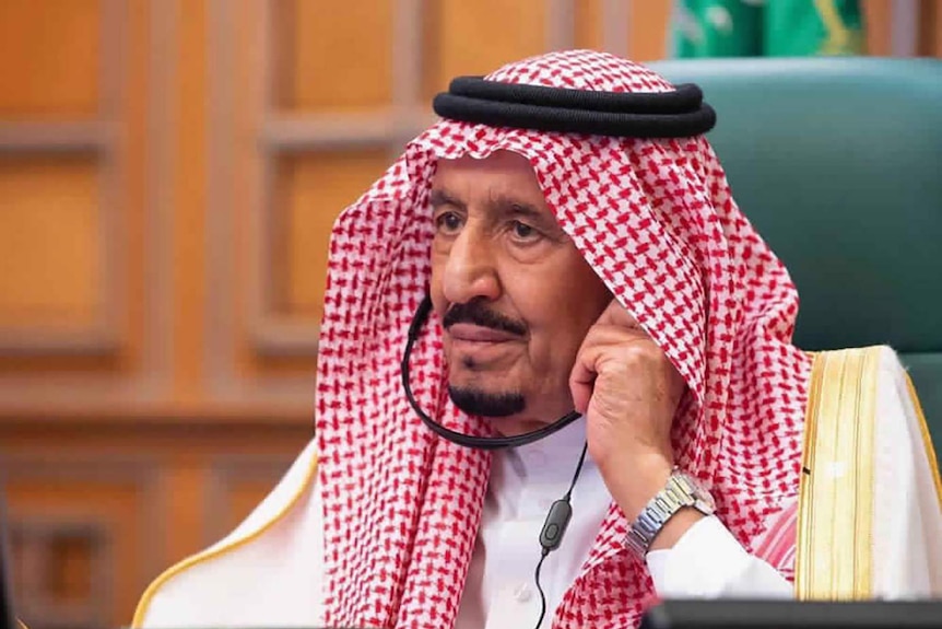 Saudi King Salman sits in a green chair wearing headphones.