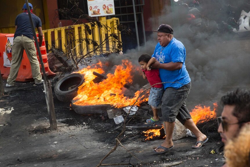A man carries a boy across a barricade of burning tyres.