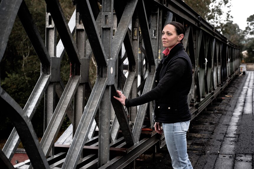 a woman standing on an old damage bridge. She is touching the bridge and looking at damage on the trusses. The bridge is closed 