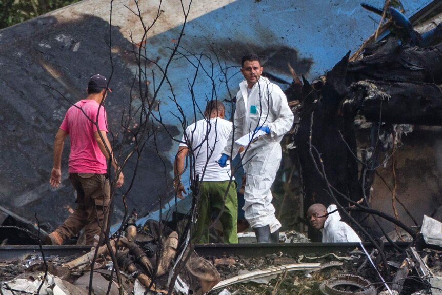 Four officials sift through the remains of the plane, near a burnt wing.