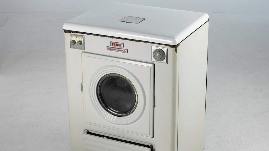 A mid-century, white Bendix washing machine is pictured in front of a scuffed white photo backdrop.