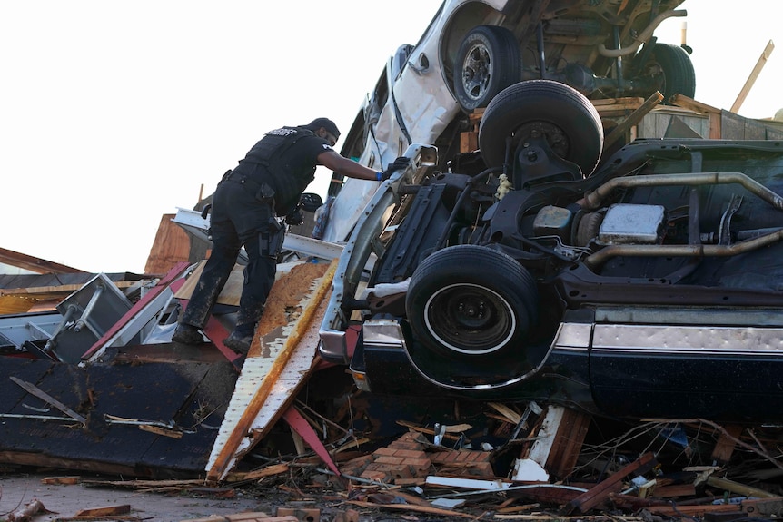 A sheriff's deputy climbs onto a pile of wind-tossed vehicles piled on top of each other.