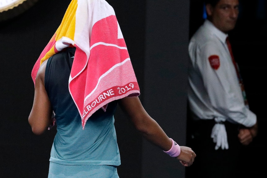Naomi Osaka walks off the court with a towel over her head.