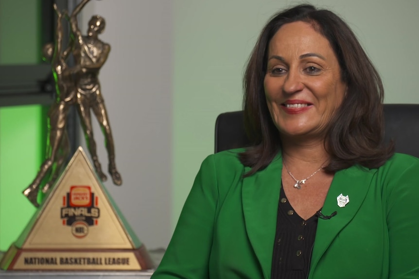 A woman with brown hair and green blazer sitting in front of a trophy