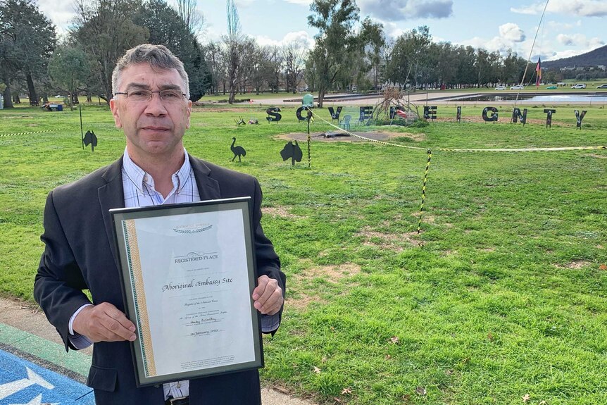 A man holds a certificate outside on a lawn.