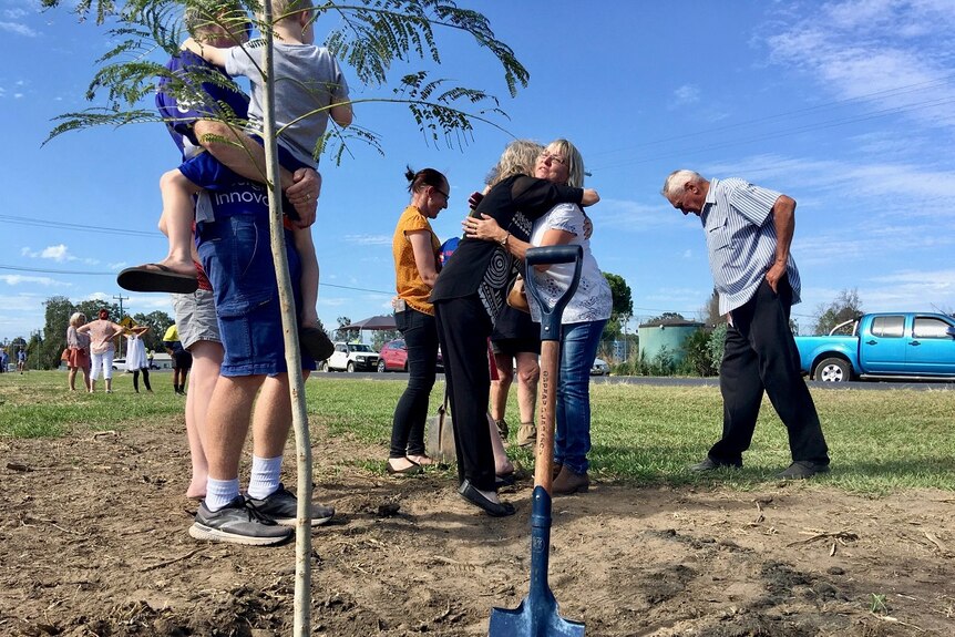 Family and friends hugging and catching up alongside a new jacaranda sapling and the spade used to plant it.