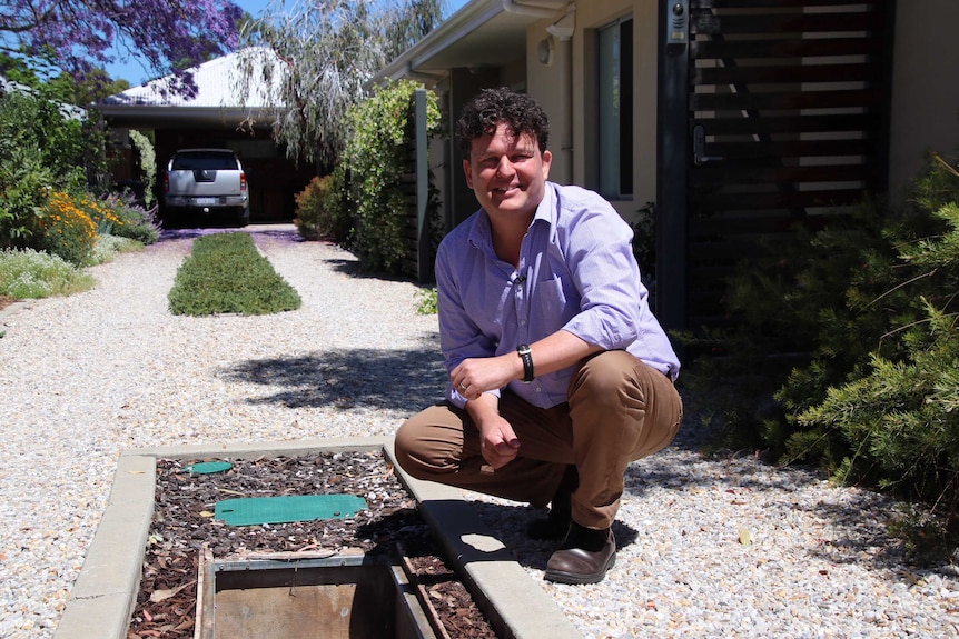 Environmental scientist and gardening presenter Josh Byrne crouches on the ground in his driveway next to a bore.