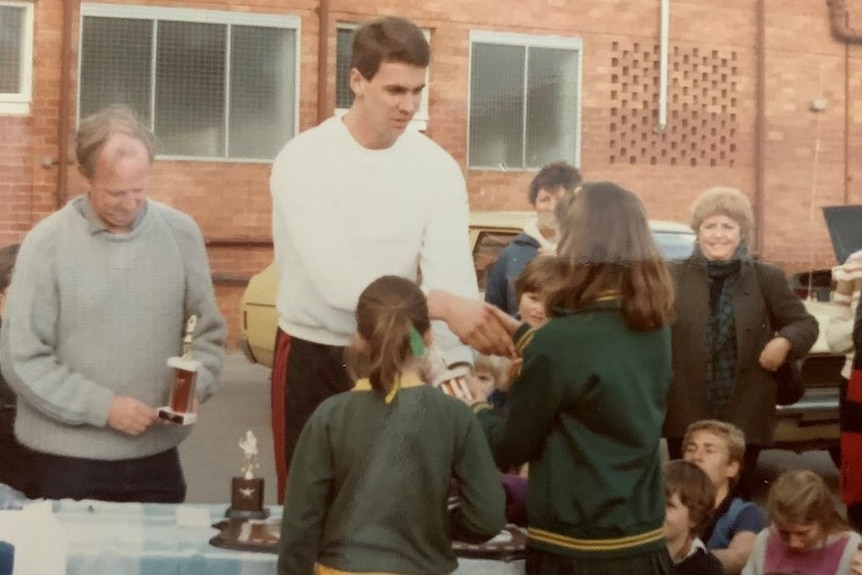 A tall man hands a primary school aged girl a trophy.
