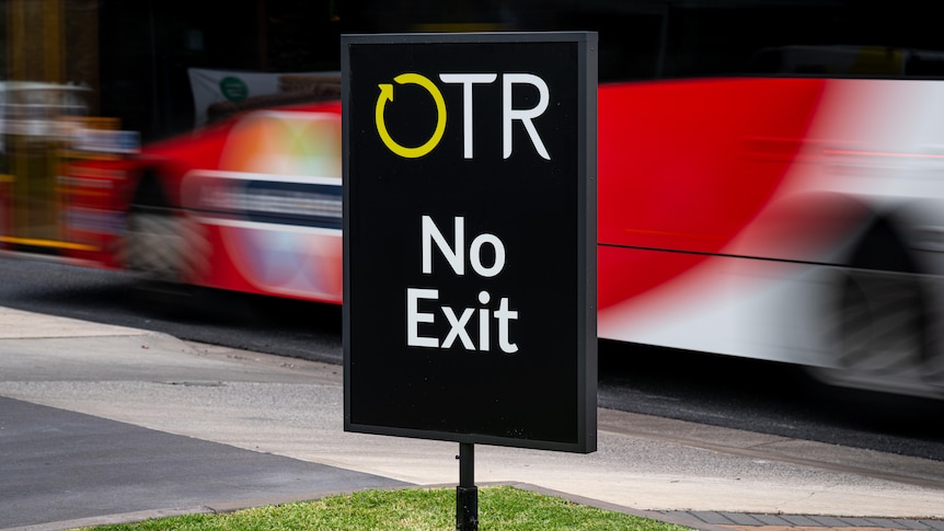 Black sign which reads OTR no exit, as a bus passes behind it.