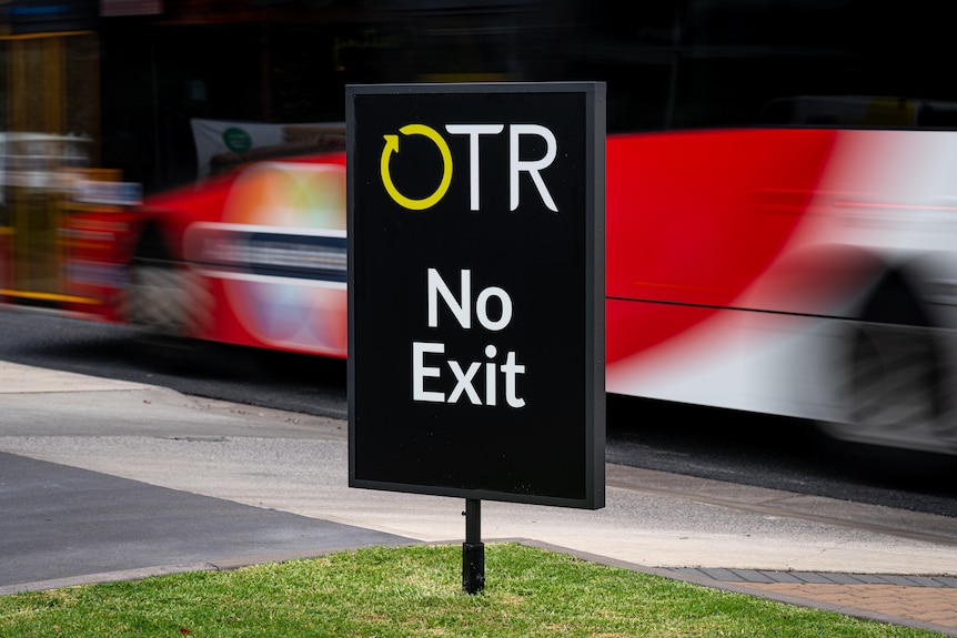 Black sign which reads OTR no exit, as a bus passes behind it.