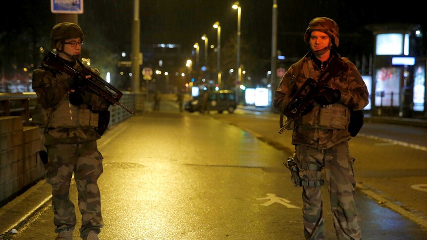 Soldiers with high-powered weapons stand guard on a street.