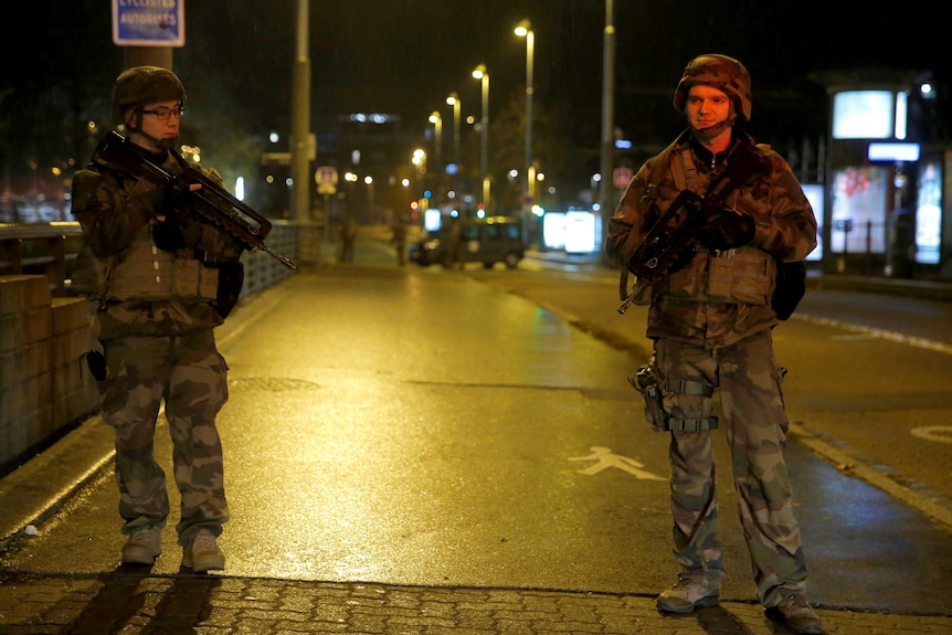 Soldiers with high-powered weapons stand guard on a street.