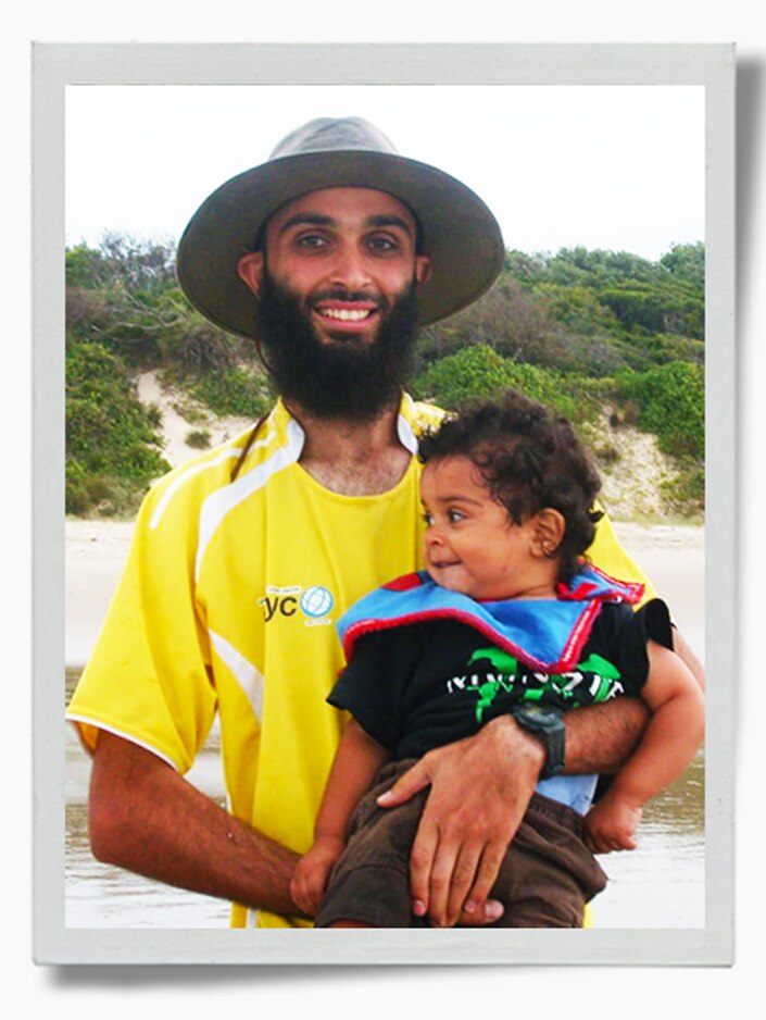 Muhammad Zahab stands at a beach holding a child.