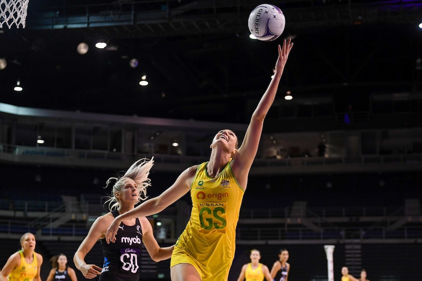 Attacking netballer reaching back for a ball thrown over her head with a defender trailing behind