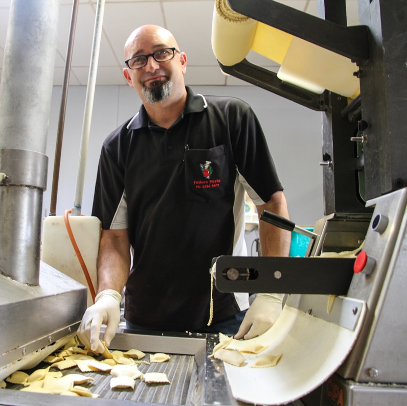 A man makes ravioli using a pasta making machine