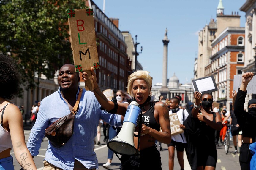 On a clear day, you view a group of people of African ancestry marching down a London street holding a sign that reads "BLM".