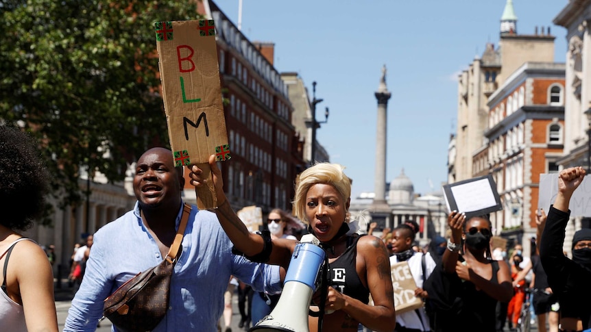 On a clear day, you view a group of people of African ancestry marching down a London street holding a sign that reads "BLM".