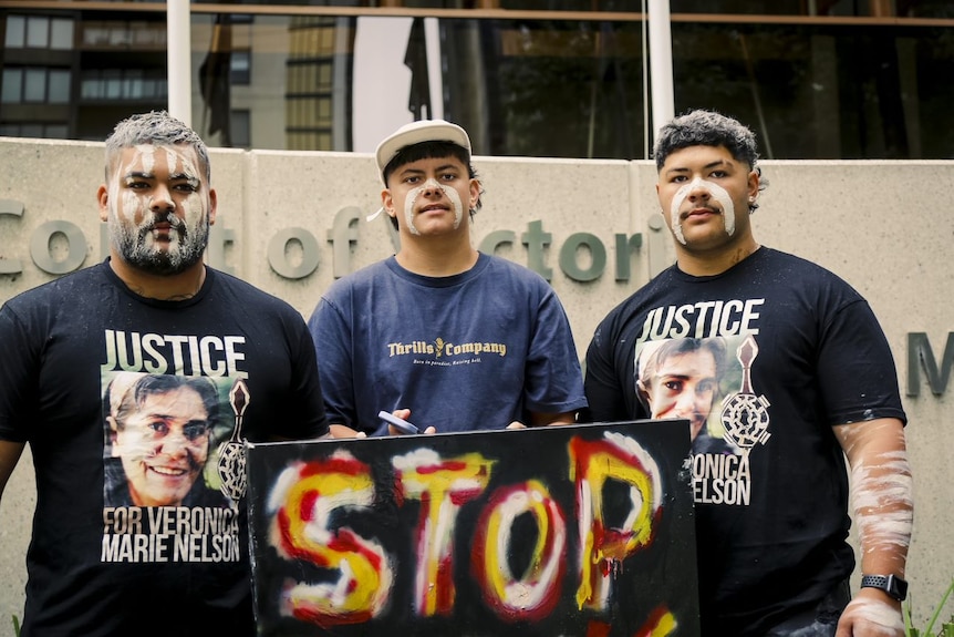 Three men with paint on her face hold a sign that says stop outside court.