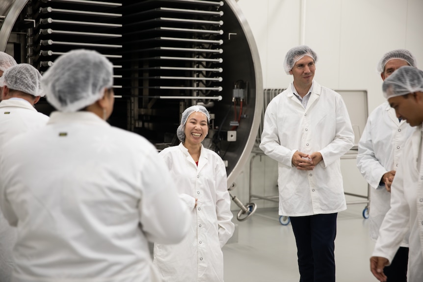 Женщина стоит с группой мужчин в белых халатах на фабрике.