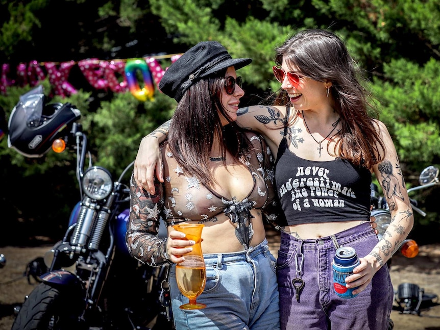 Two women arm in arm smile at each-other