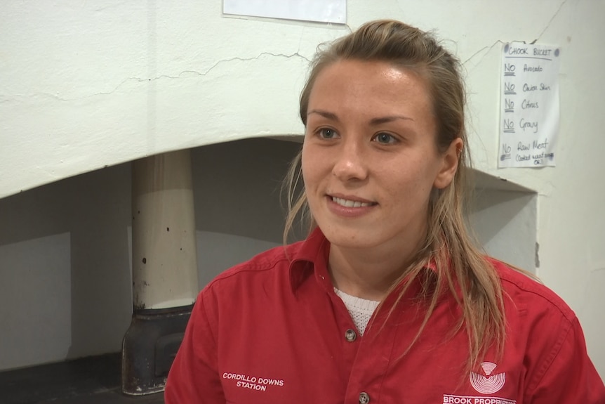 A young lady with blonde hair stares away from the camera.  She is wearing a red shirt.