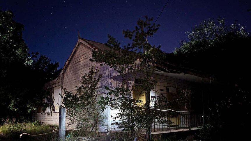 Cantle's Cottage at night before it burned down surrounded by trees, with light shining off its wooden boards.
